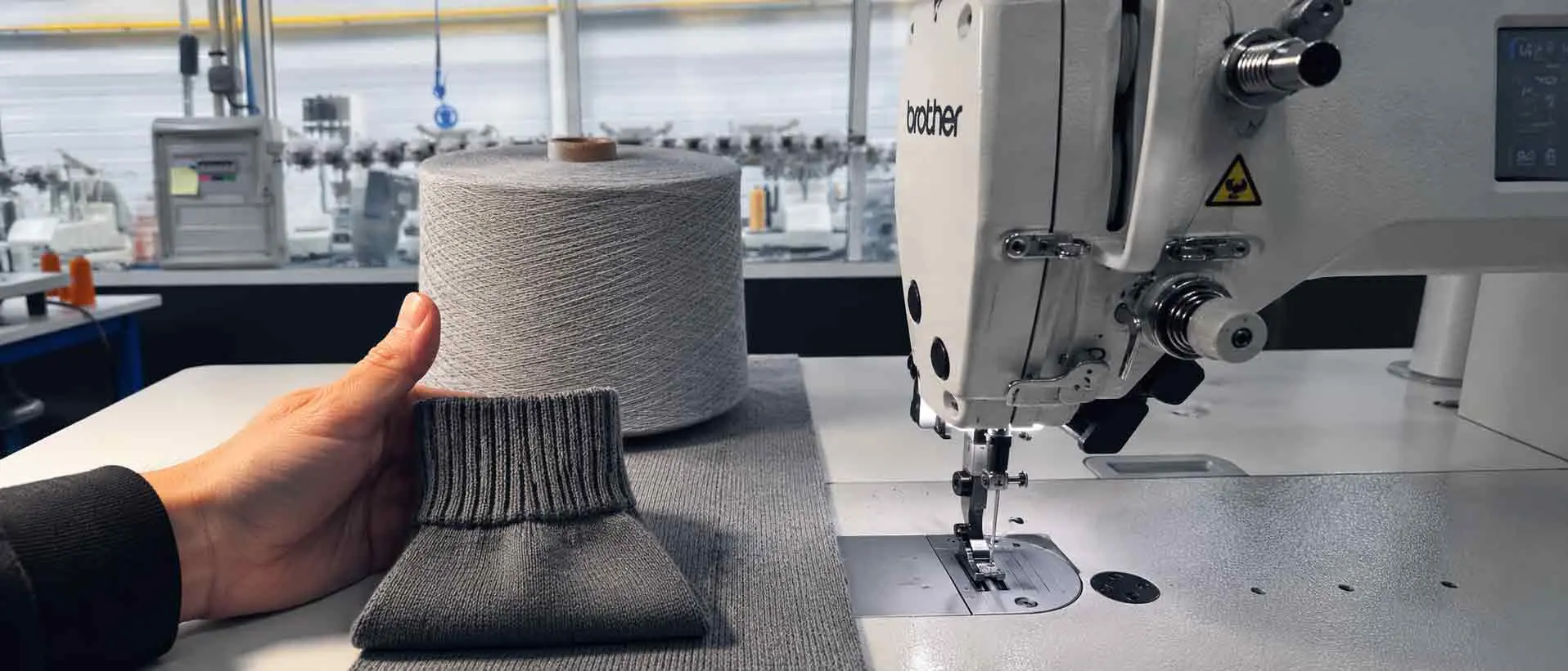 Dans l’atelier PELOT à Vire : une main présente une maille, un cône de fil et une machine de confection.