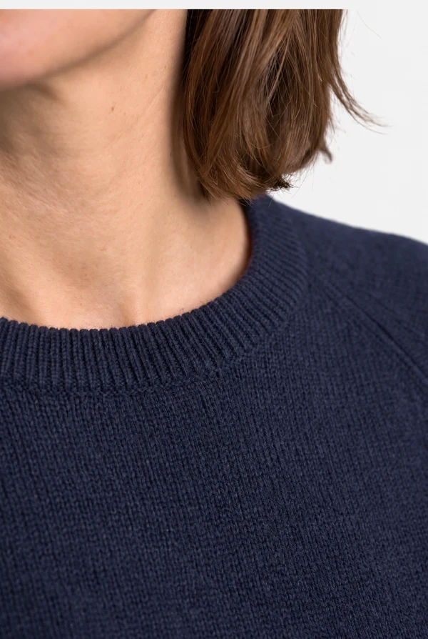 Detail of the ribbed crew neck and raglan sleeve of the PELOT made-to-measure sweater, worn by a woman.
